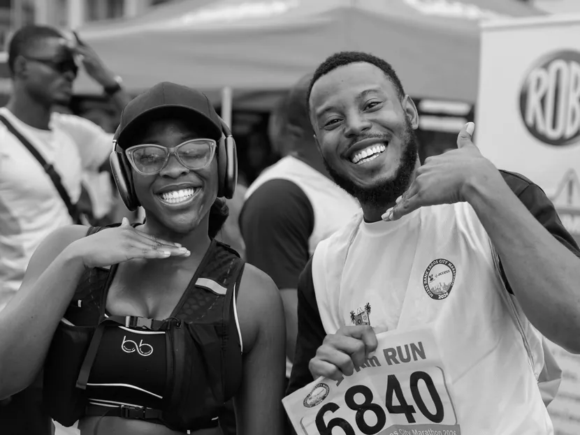 Stock photo in black and white: two runners wearing race numbers smile and pose at a city race.